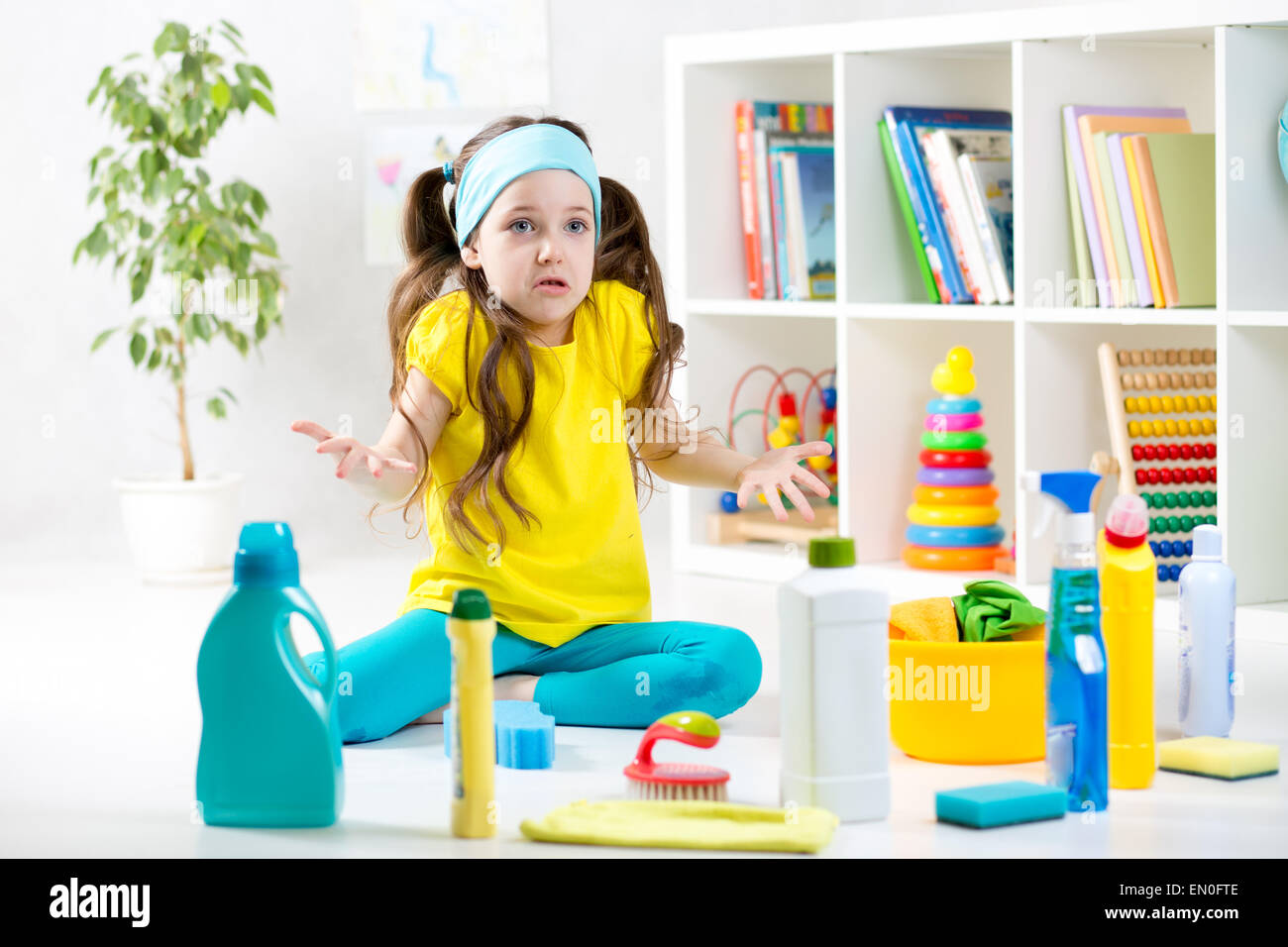 Frustrati kid ragazza seduta sul pavimento con strumenti di pulizia Foto Stock