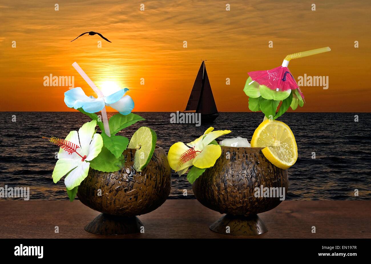 Cocktail di frutta guarnire e cannucce floreale con tramonto e barca a vela vela sull'acqua. Foto Stock