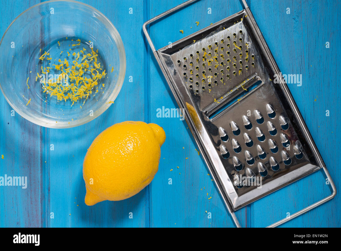 Limone, ciotola e grattugia su una scheda blu Foto Stock