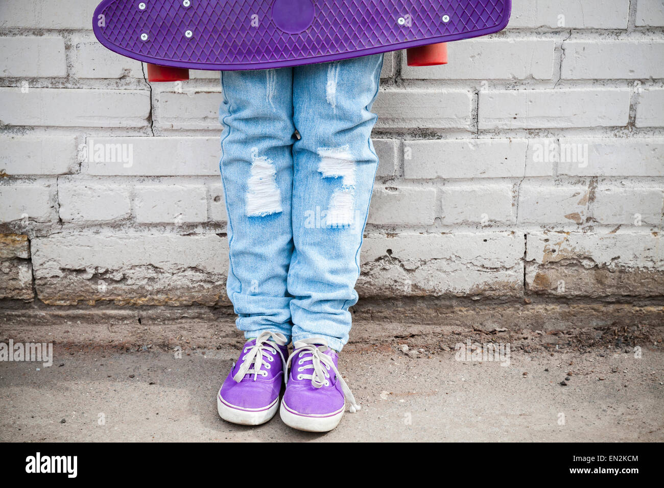 Adolescente in blue jeans e gumshoes stand con lo skateboard in prossimità urbano grigio muro di mattoni Foto Stock