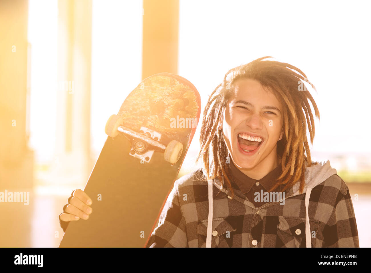 Ritratto di giovane ragazzo con lo skateboard e capelli rasta in un concetto di stile di vita caldo filtro applicato Foto Stock
