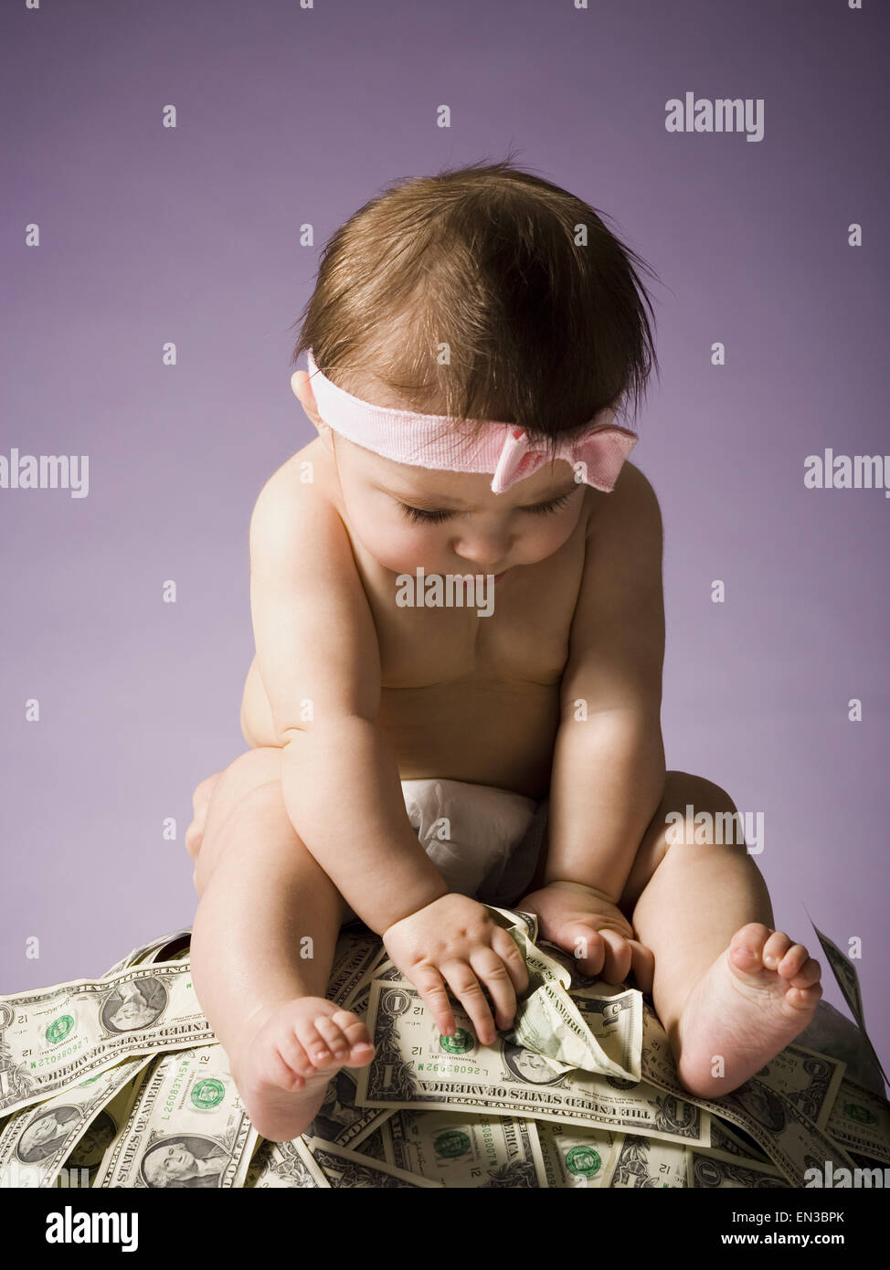 Baby ragazza seduta sulla pila di valuta statunitense Foto Stock