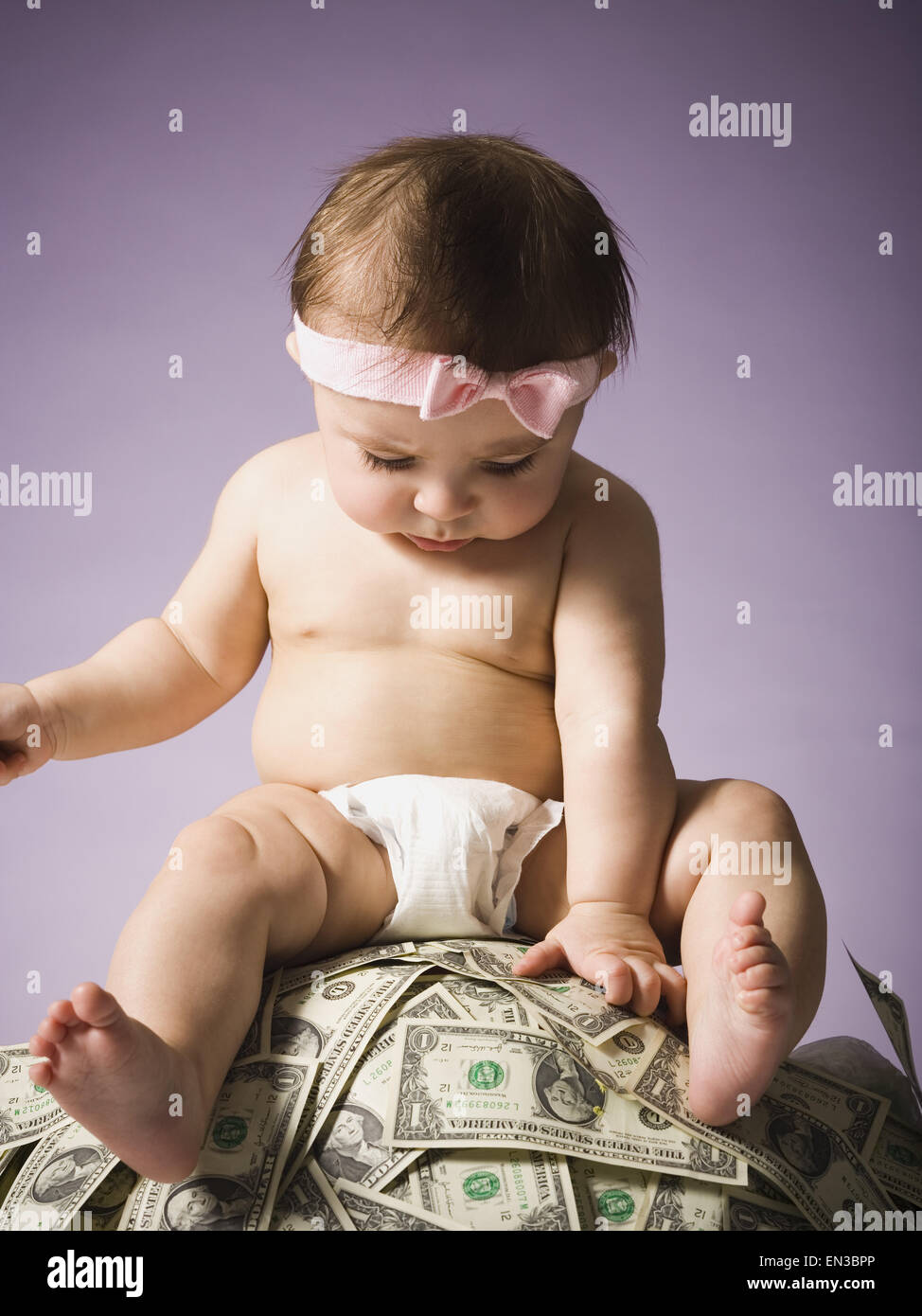Baby ragazza seduta sulla pila di valuta statunitense Foto Stock
