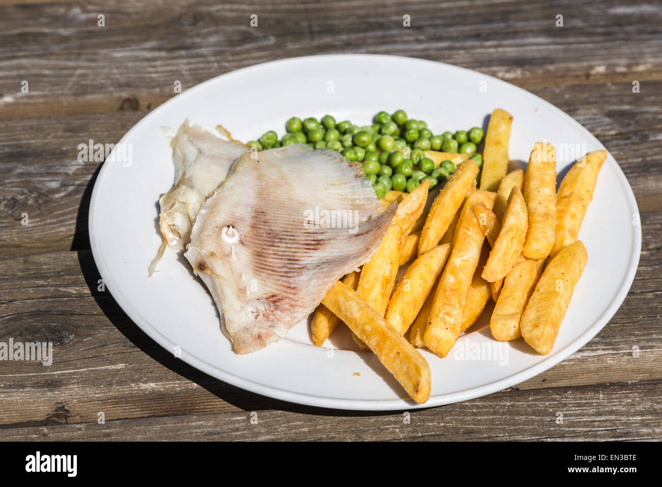 Pasto di skate ala, golden chip e piselli verdi su una piastra bianca su una tavola di legno Foto Stock