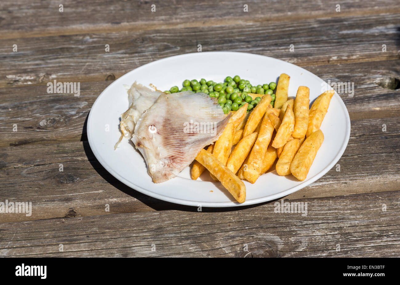 Pasto di skate ala, golden chip e piselli verdi su una piastra bianca su una tavola di legno Foto Stock