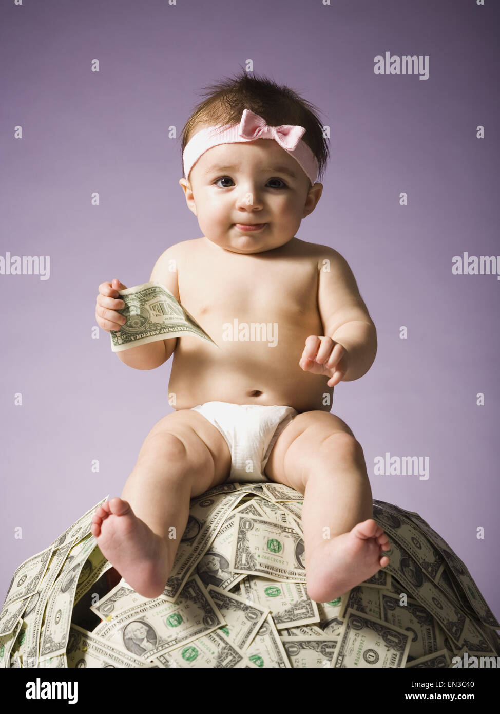 Baby ragazza seduta sulla pila di valuta statunitense Foto Stock