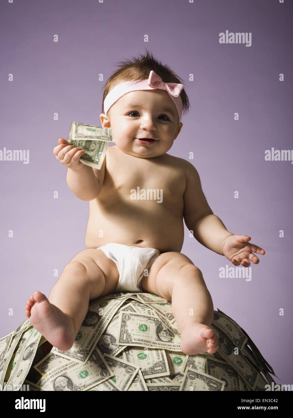Baby ragazza seduta sulla pila di valuta statunitense Foto Stock