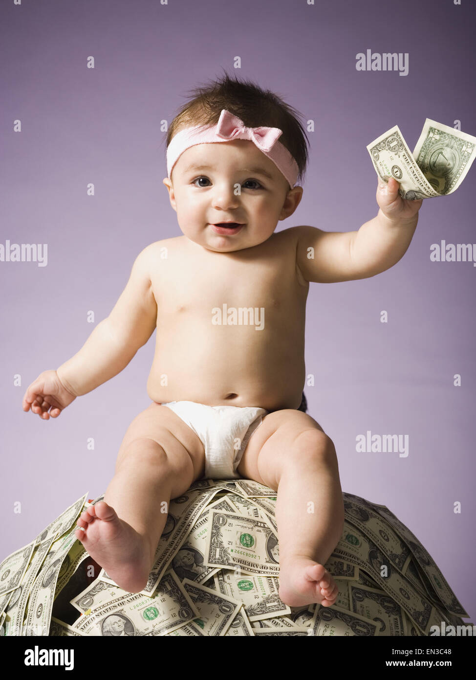 Baby ragazza seduta sulla pila di valuta statunitense Foto Stock