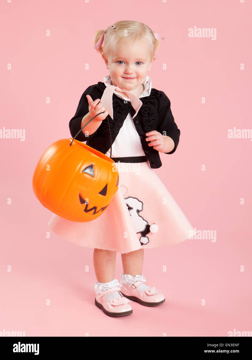 Baby girl (12-17 mesi) negli anni cinquanta il costume di stile, tenendo zucca lanterna per Halloween Foto Stock