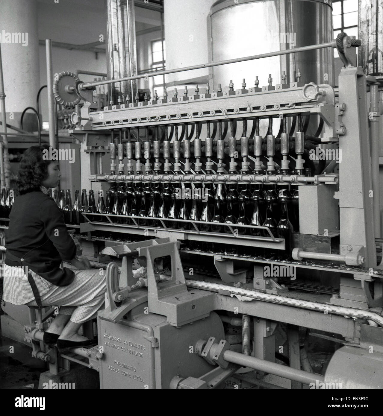 Anni '50, giovane operatrice femminile che lavora in un coperchio di imbottigliamento in metallo o una macchina per tappare bottiglie, Hong Kong. Foto Stock