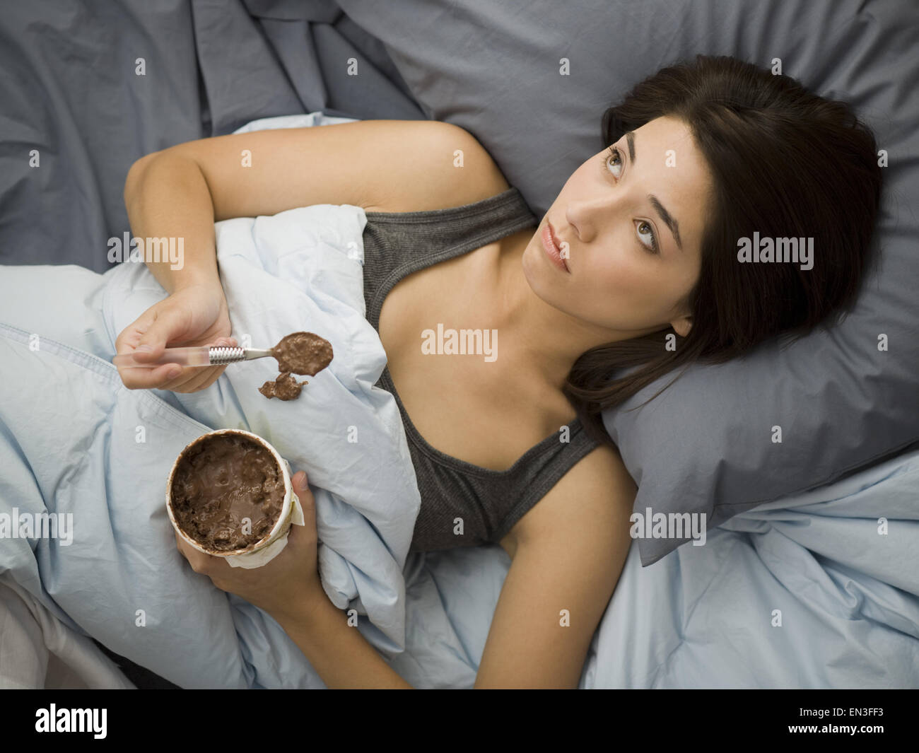 Donna sdraiata nel letto fuoriuscita di gelato al cioccolato sulla coperta Foto Stock