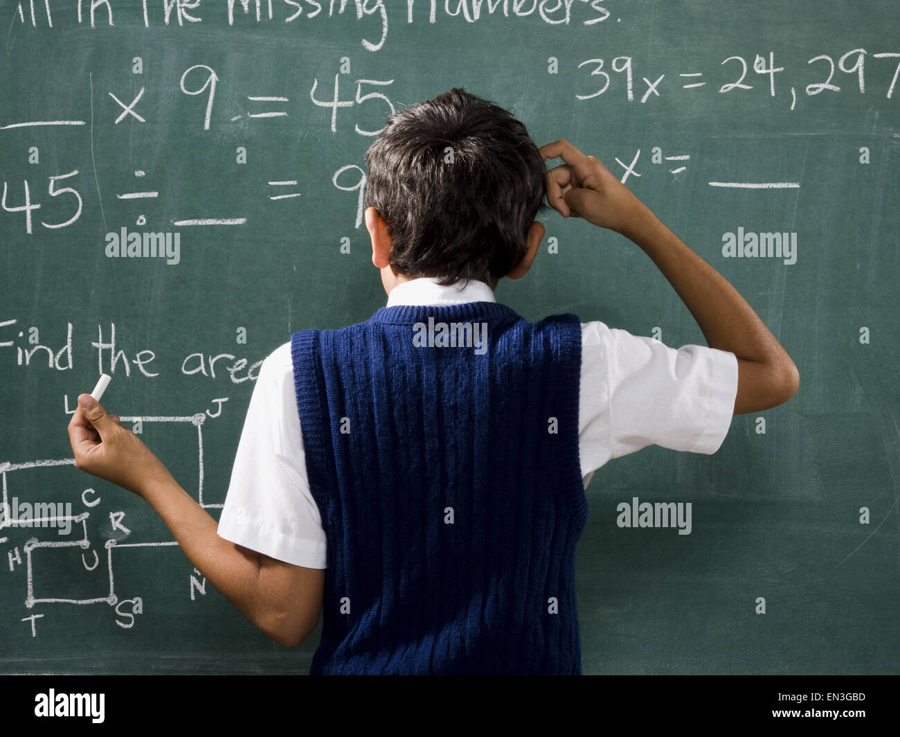 Vista posteriore del ragazzo in chalkboard facendo le formule matematiche e graffiare la testa Foto Stock