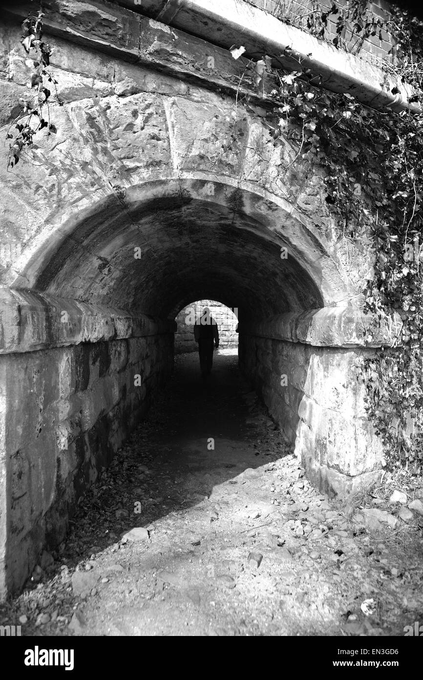 Silhouette di un uomo a piedi attraverso un vecchio tunnel sotto un ponte ferroviario Foto Stock