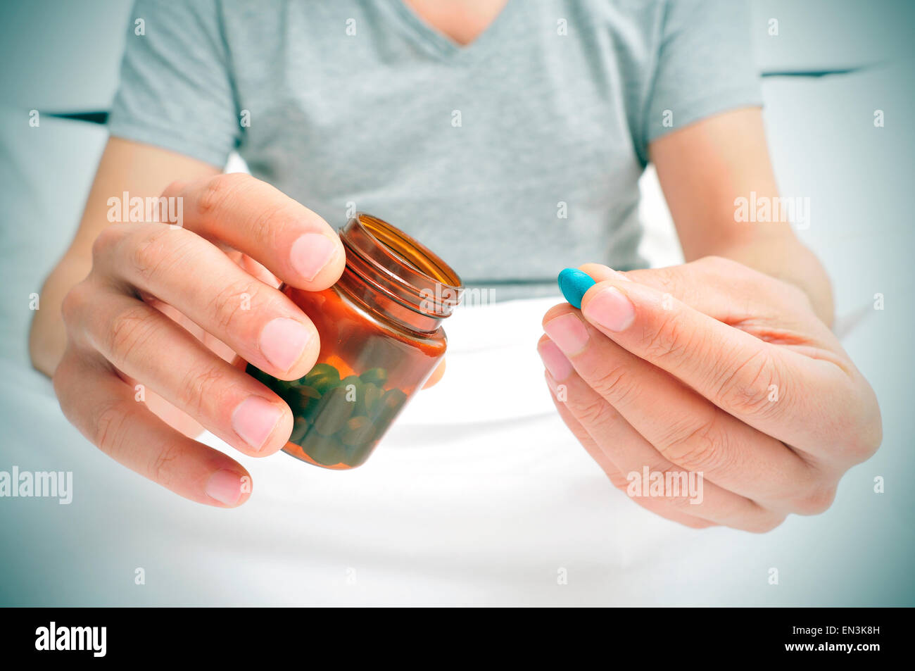 Un giovane uomo caucasico in pigiama nel letto in procinto di prendere la pillola blu da una bottiglia marrone Foto Stock