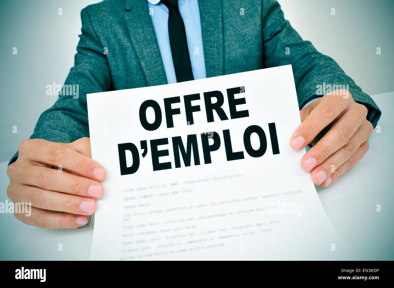 Primo piano di un giovane uomo in abito grigio seduta nel suo ufficio che mostra un documento con il testo offres d'emploi, lavori in francese, Foto Stock