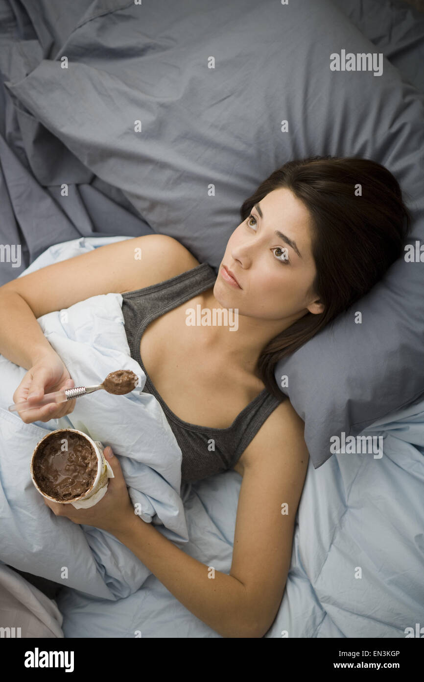 Donna giaceva a letto a mangiare il gelato al cioccolato Foto Stock