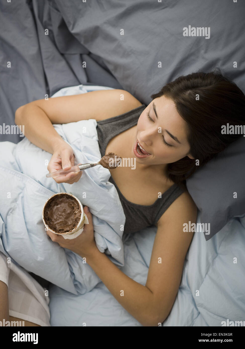 Donna giaceva a letto a mangiare il gelato al cioccolato Foto Stock