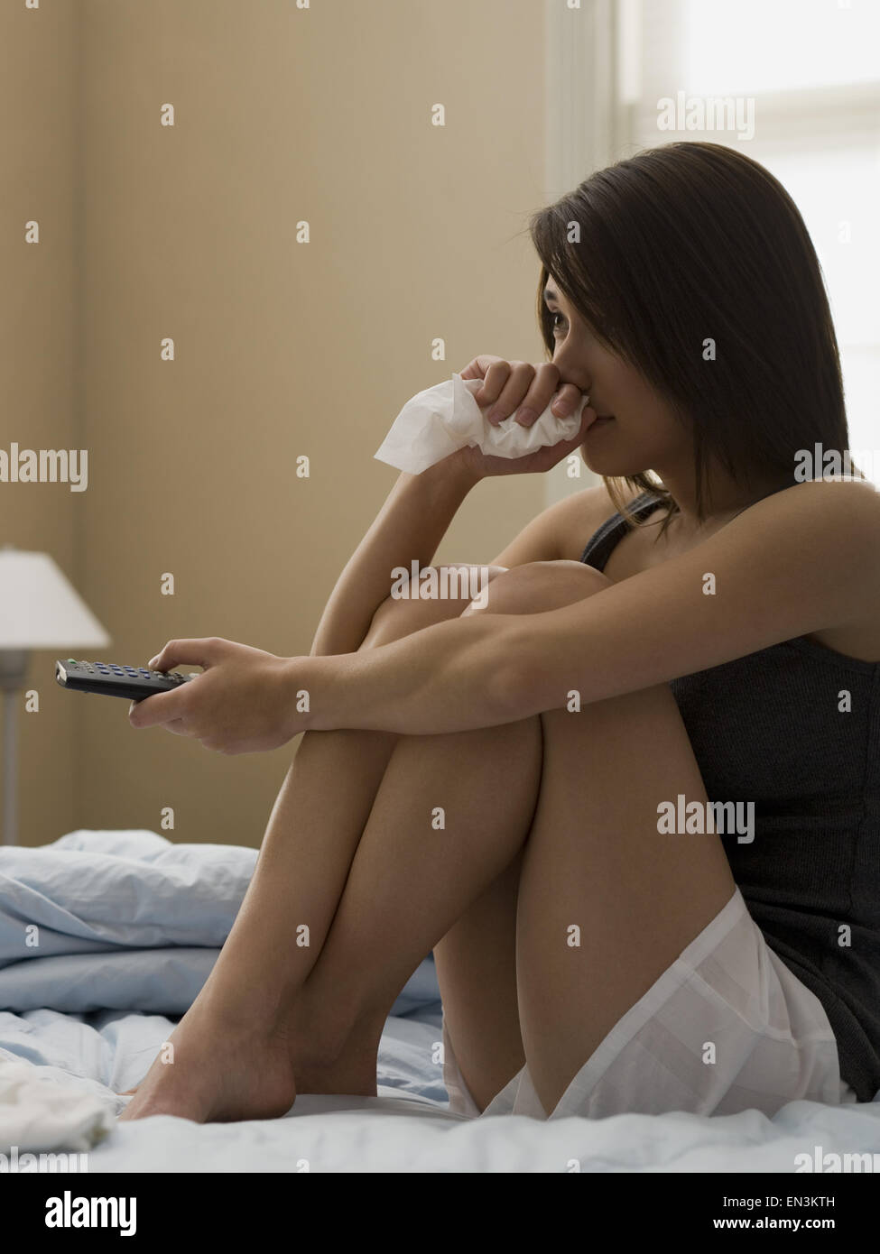 Donna seduta sul letto di televisione con telecomando e il tessuto Foto Stock