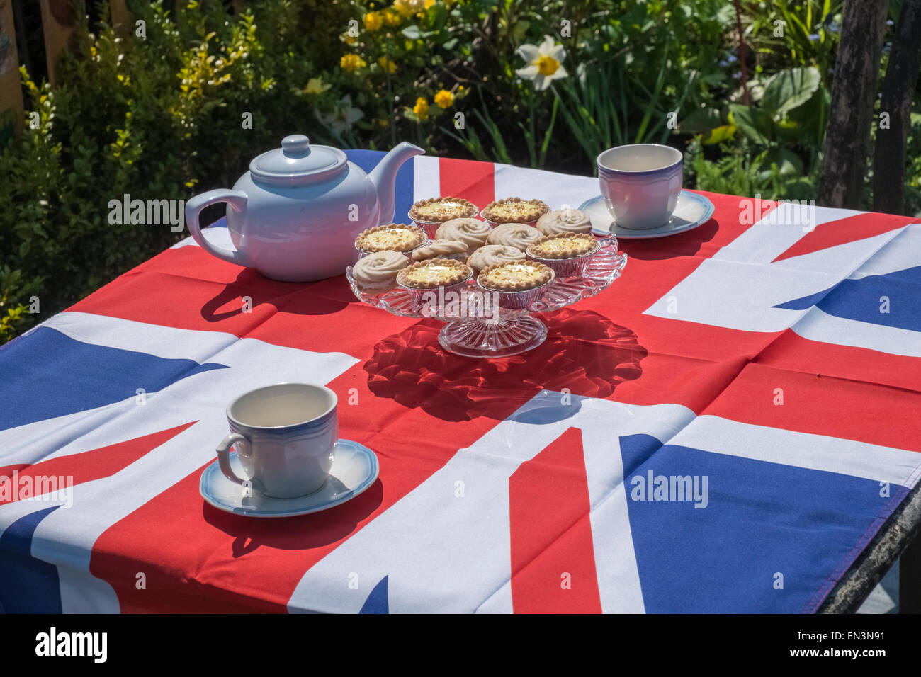 Il tè del pomeriggio teiera e teacups con scelta di dolci, steso su una bandiera europea tovaglia. Foto Stock