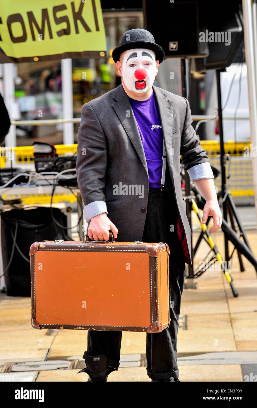 Clown con il bianco faccia dipinta, naso rosso che indossa un cappello e porta con sé una valigia in The Guildhall Square, Derry, Londonderry, Nort Foto Stock
