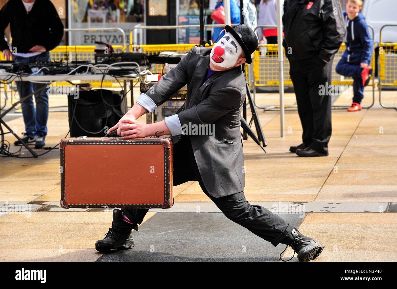 Clown con il bianco faccia dipinta, naso rosso che indossa un cappello e porta con sé una valigia in The Guildhall Square, Derry, Londonderry Foto Stock