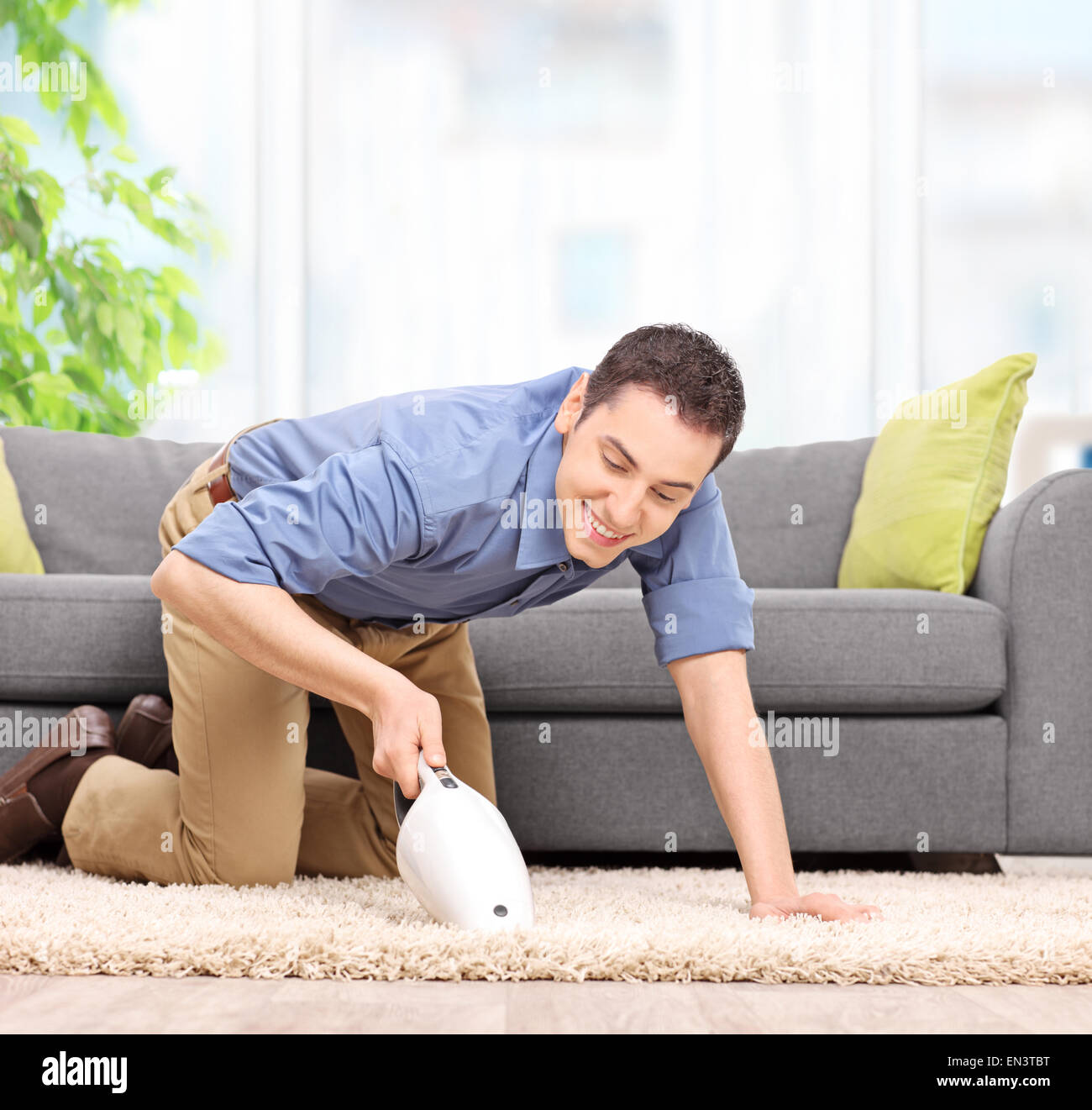 Giovane uomo aspira un tappeto con un palmare aspirapolvere e sorridente a  casa Foto stock - Alamy