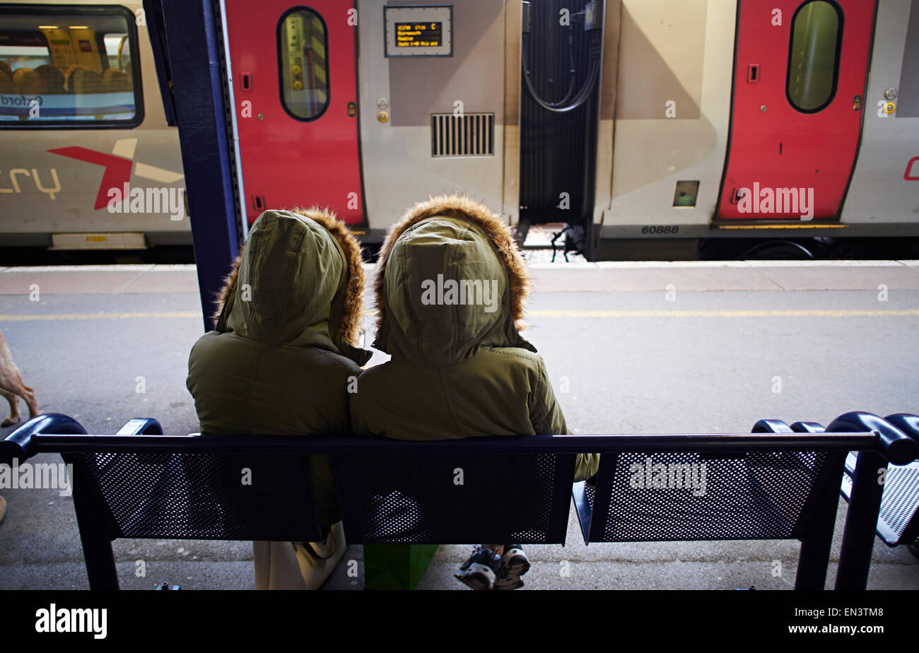 Gemello ragazze nella stessa parker rivestire in attesa del treno alla stazione di Oxford. Foto Stock