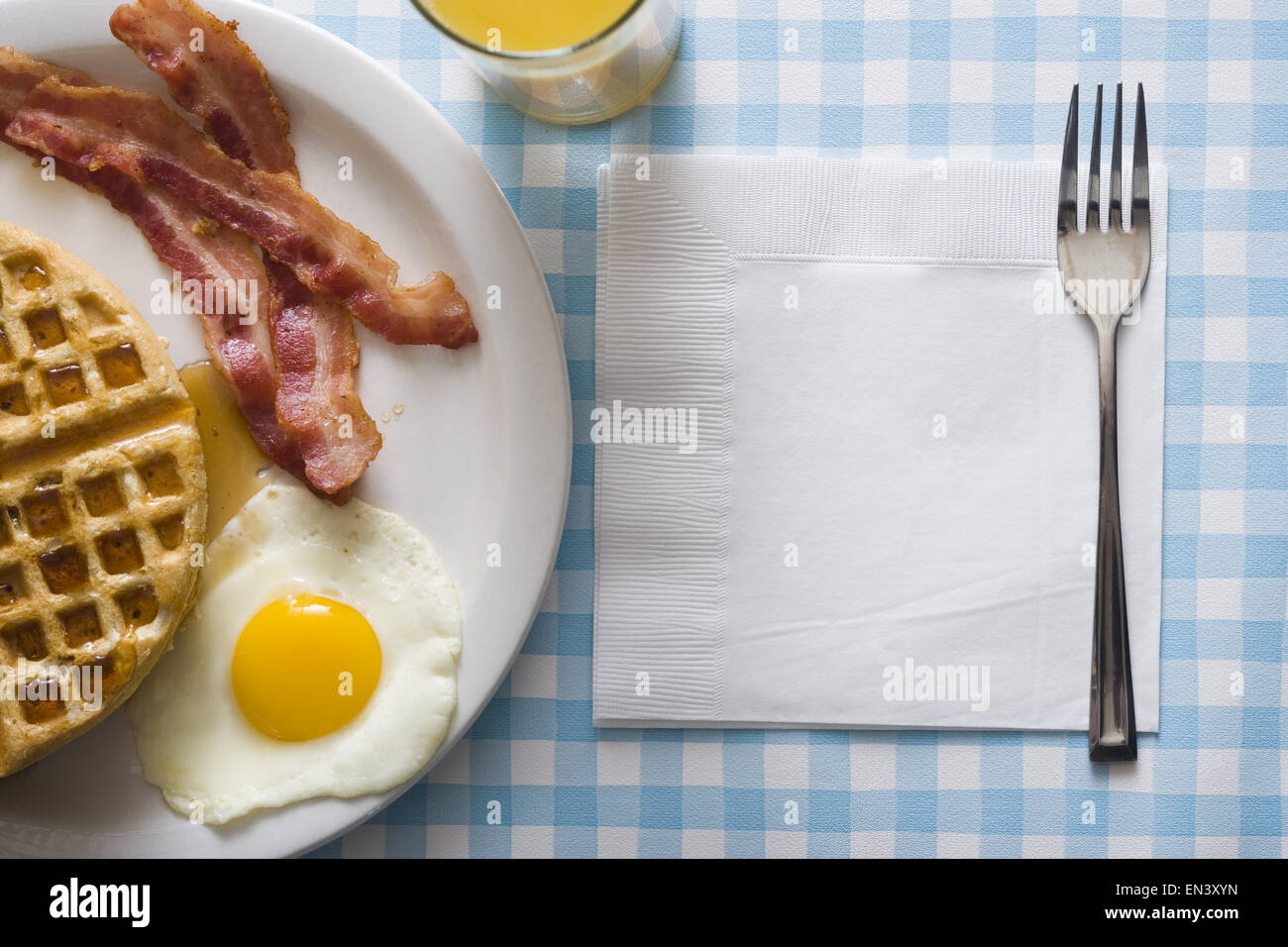 Uova e pancetta con waffle e succo d'arancia con igienico e forcella Foto Stock
