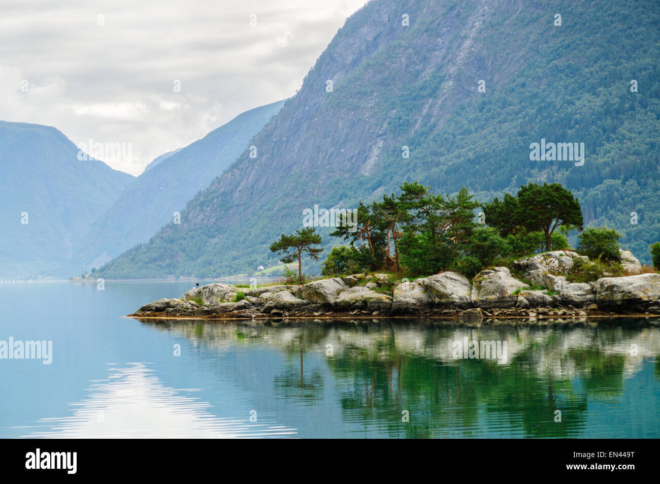 Piccola e rocciosa isola di pino con le montagne sullo sfondo a fiordo norvegese Foto Stock