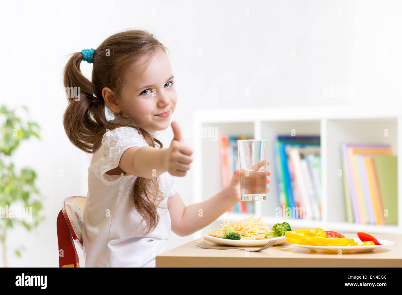 Bambino mangia il cibo sano che mostra il pollice in alto Foto Stock