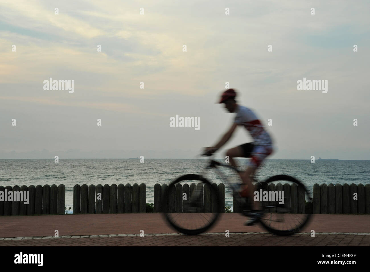 Movimento dei singoli maschio adulto ciclista MTB equitazione bicicletta sul lungomare accanto all'oceano all'alba, il lungomare di Durban, KwaZulu-Natal, Sud Africa Foto Stock