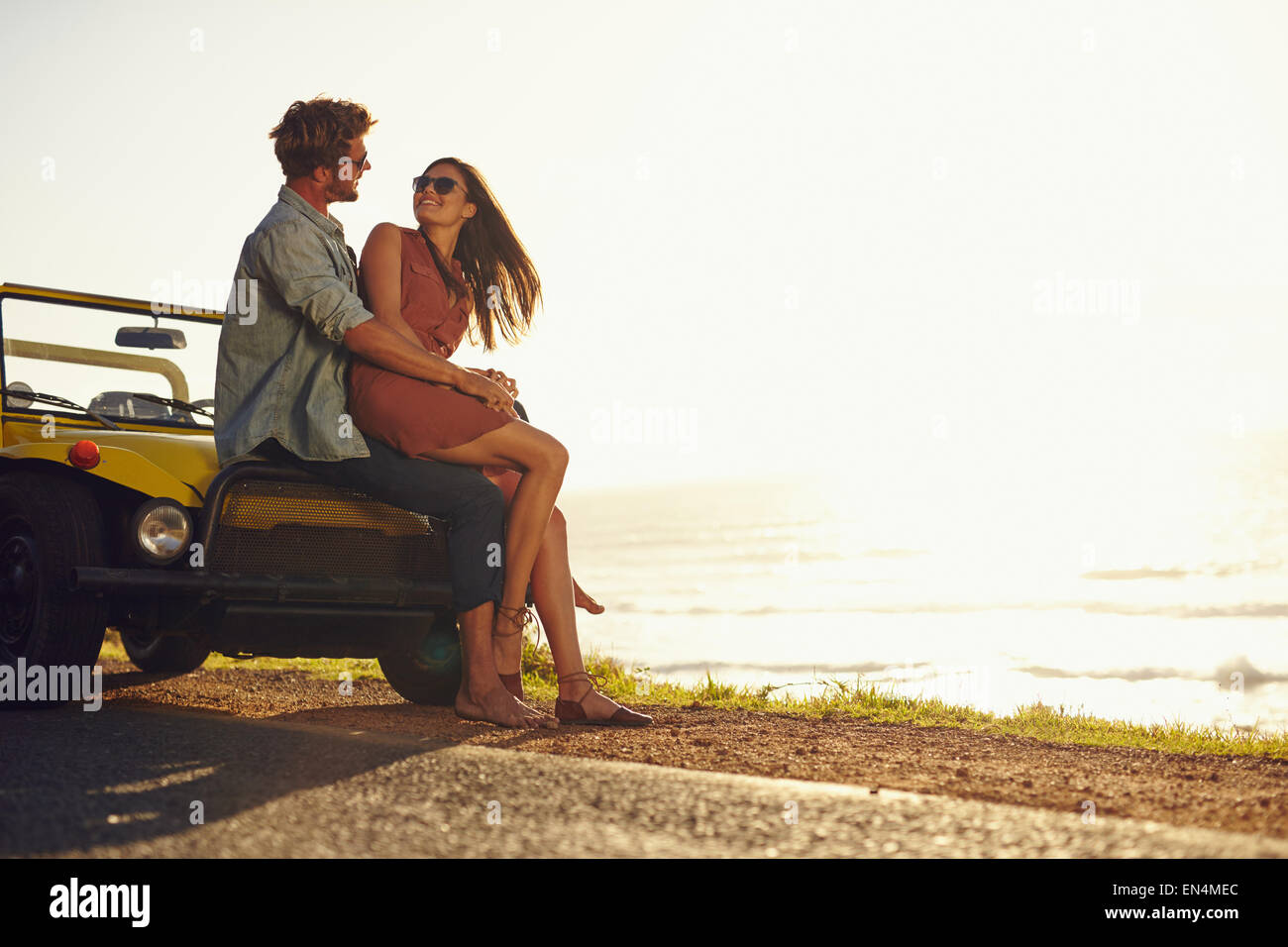 Coppia giovane che ognuno guarda negli occhi dell'altro. Romantico coppia giovane seduto sul cofano della loro auto godendo il momento. Foto Stock
