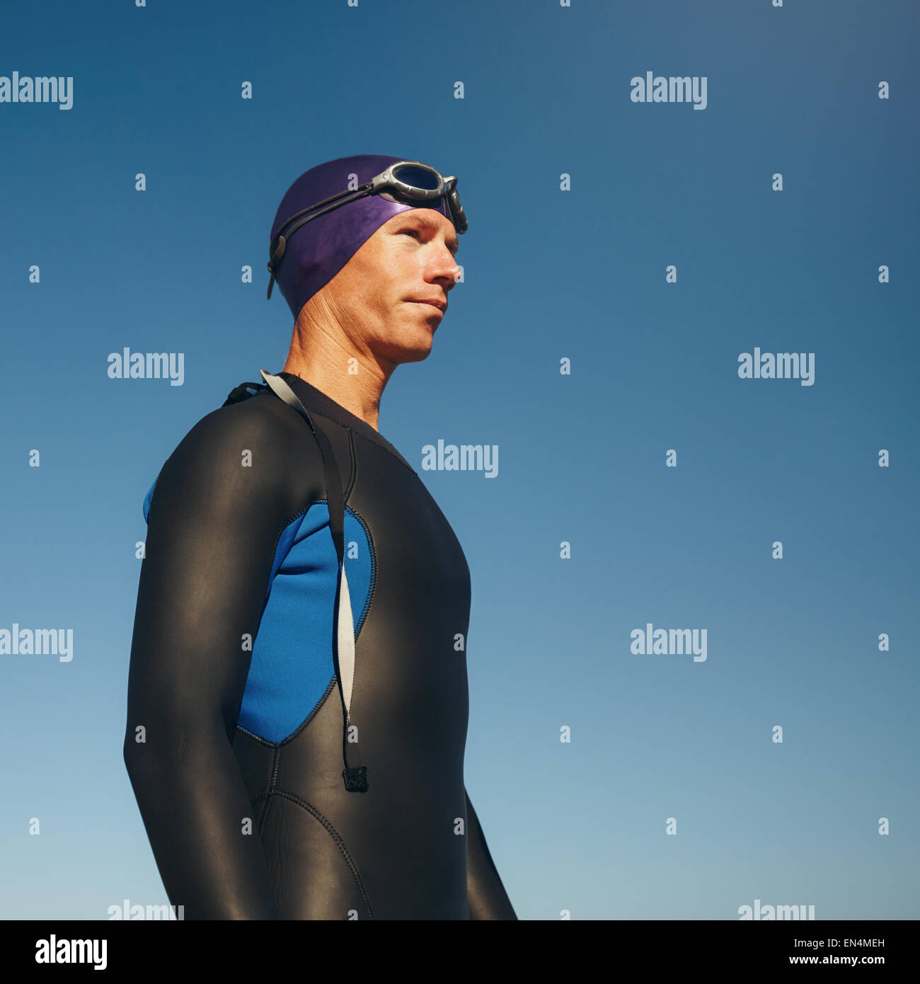 Foto di un determinato triatleta maschio che guarda lontano contro il cielo blu. Giovane uomo indossando muta pronto per il triathlon concorso Foto Stock