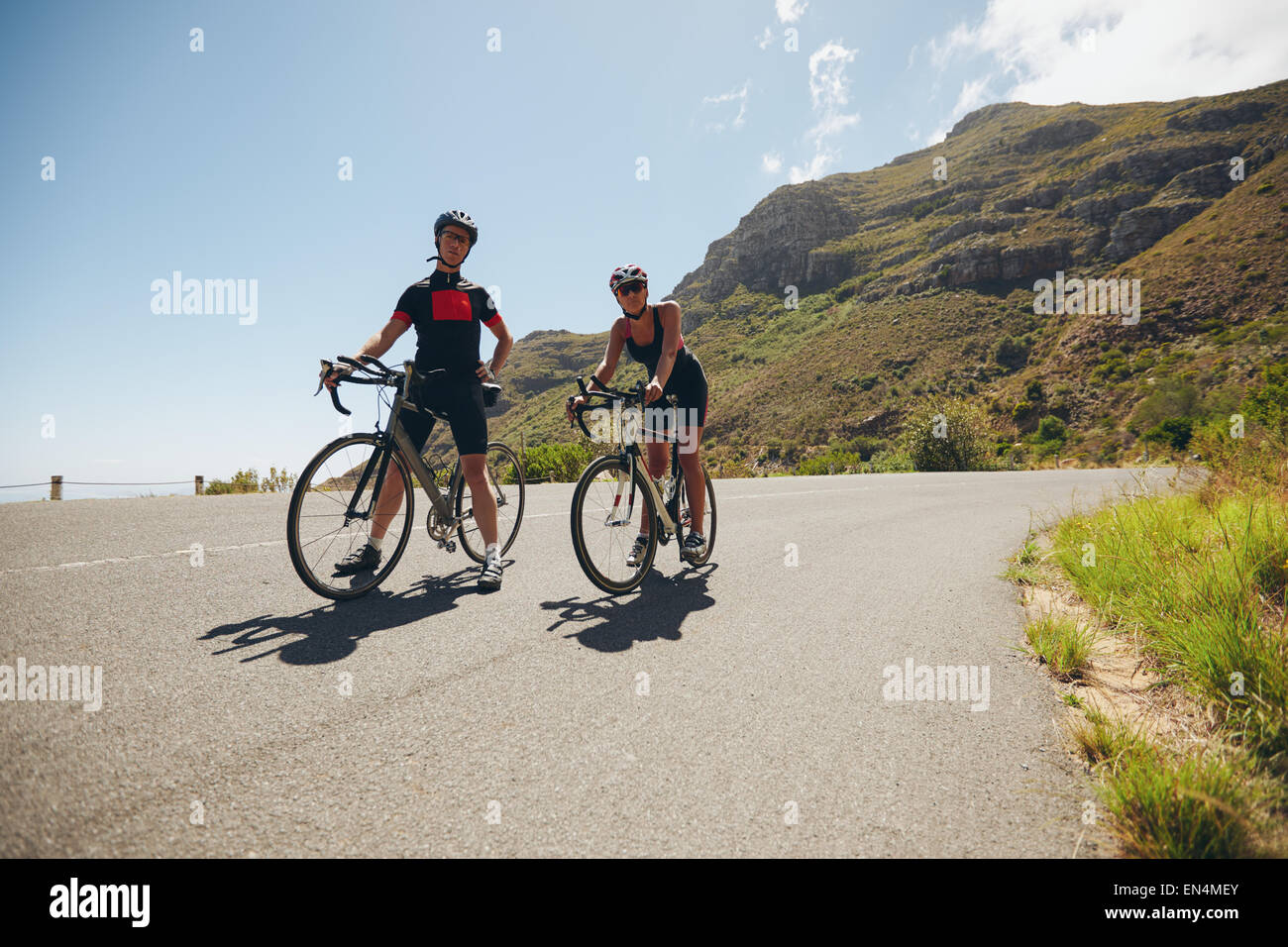 Due giovani atleti di prendere una pausa dal ciclismo su strada di campagna. Ciclista per formazione di triathlon sulla strada aperta con bic Foto Stock