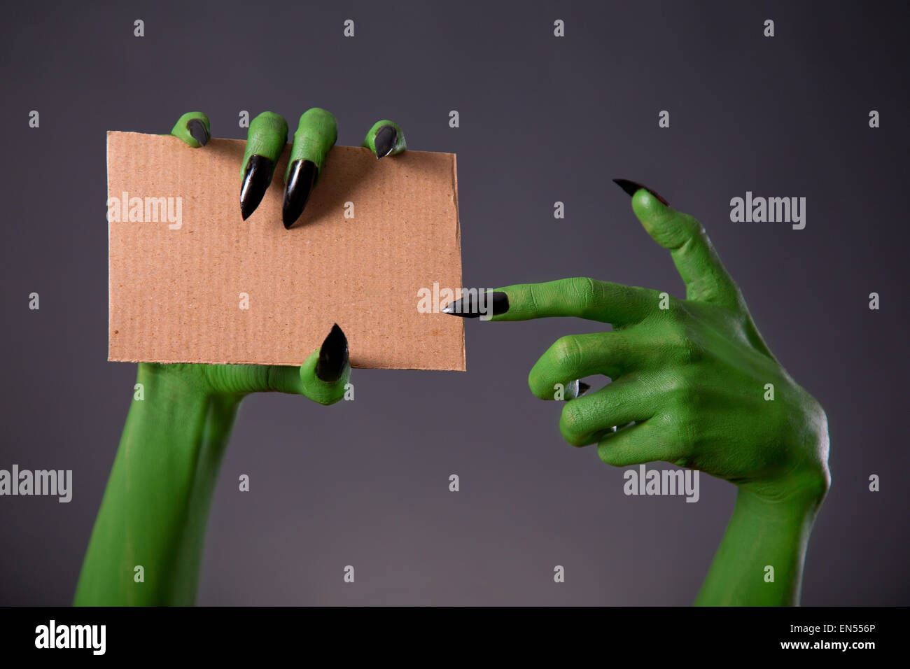 Green monster mani con nero a lungo chiodi puntando sul pezzo di cartone, tema Halloween Foto Stock