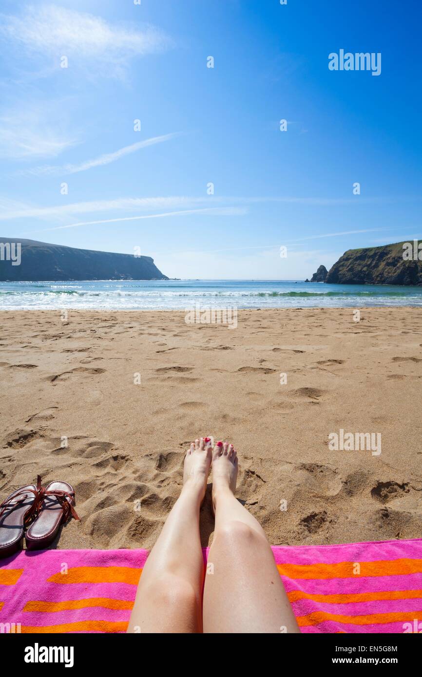 Gambe in un colorato telo mare su di una spiaggia di sabbia con vista sul mare Foto Stock