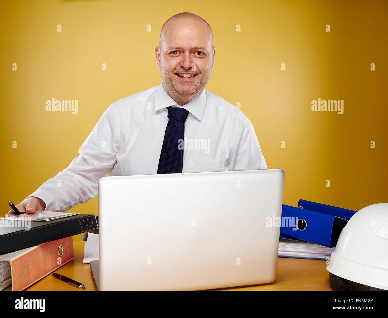 Laboriosa ingegnere maschio in ufficio egli indossa una camicia bianca e cravatta, il laptop, leganti e bianco elmetto è sul tavolo Foto Stock