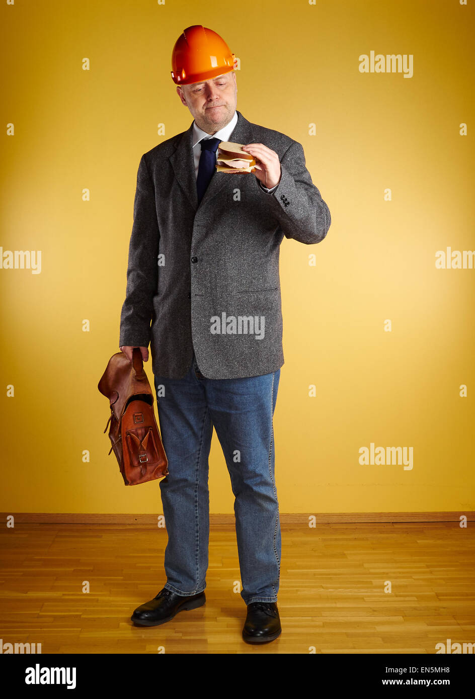 Ingegnere maschio in camera, mangia il panino e detiene vecchia valigetta in pelle, pavimenti in parquet e di parete di colore giallo Foto Stock