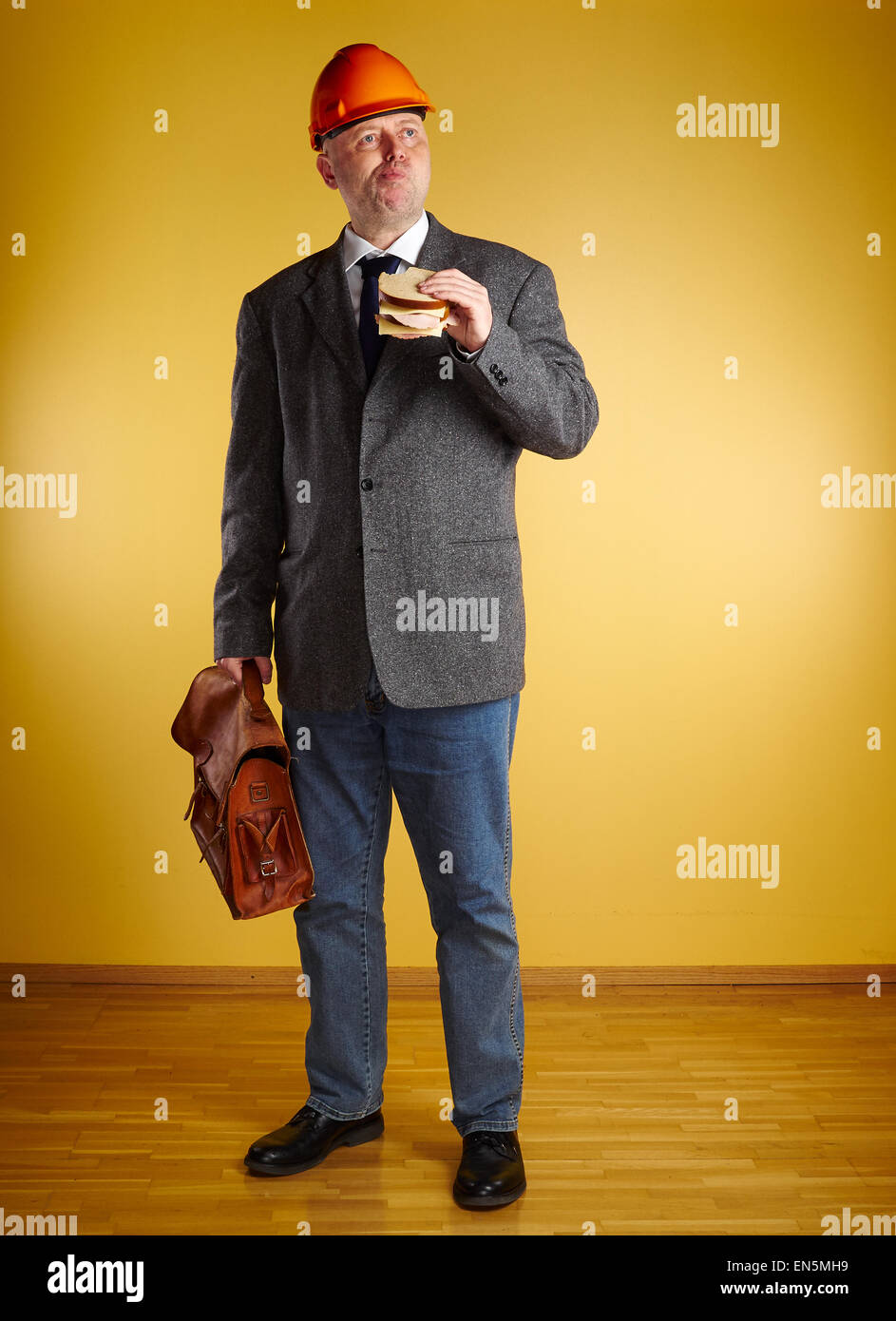 Ingegnere maschio in camera, mangia il panino e detiene vecchia valigetta in pelle, pavimenti in parquet e di parete di colore giallo Foto Stock