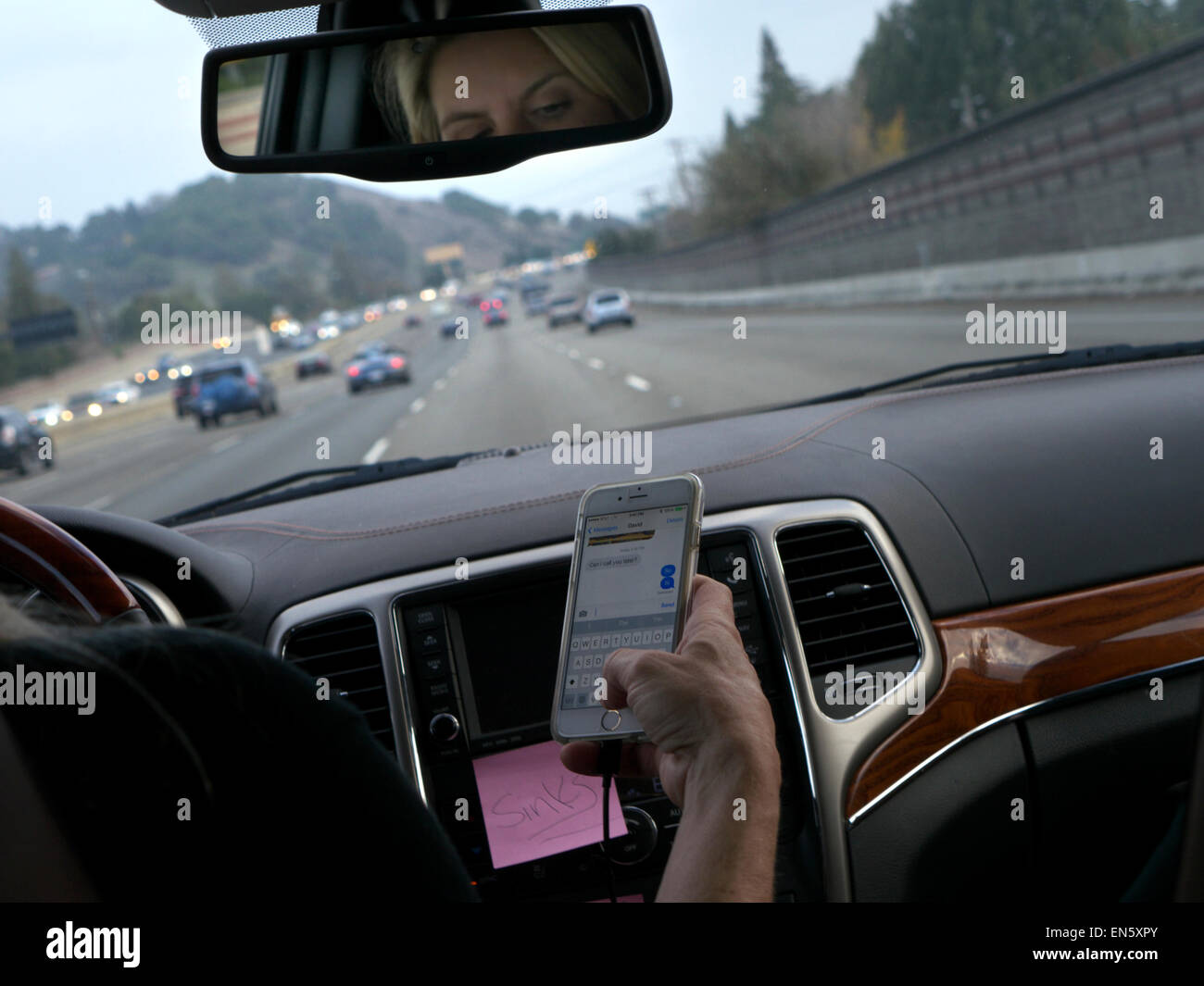 Scrivere la guida usa il driver femminile in l/h guidare il veicolo texting con iPhone smartphone durante la guida su occupato Interstate Highway California USA Foto Stock