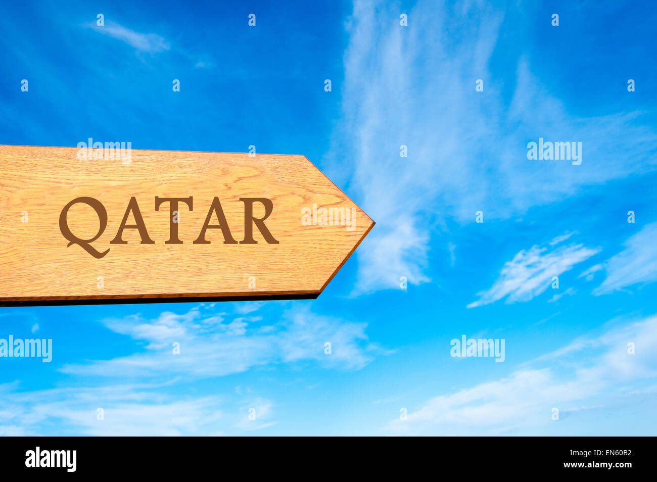 Freccia in legno cartello che indica la destinazione QATAR contro il cielo blu chiaro con copia spazio disponibile. Destinazione di viaggio immagine concettuale Foto Stock