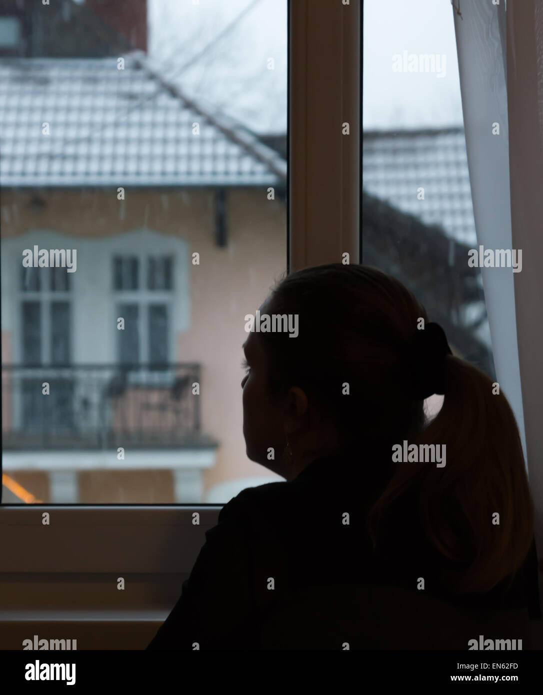 La silhouette della ragazza che si siede davanti a una finestra e guarda lontano. Foto Stock