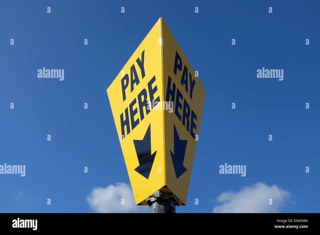 Giallo pagare qui segno contro un cielo azzurro sfondo con spazio di copia Foto Stock