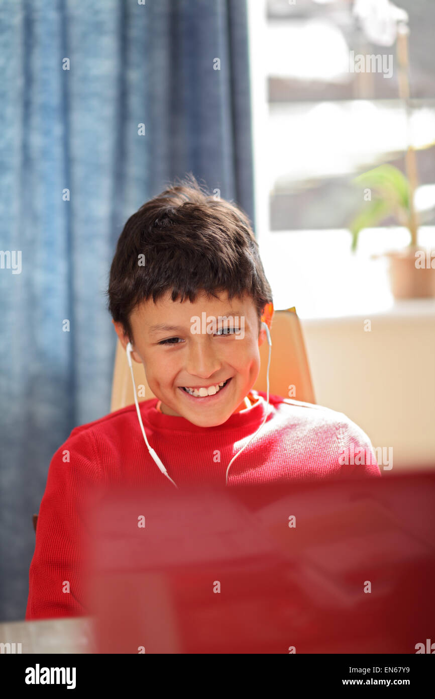 Giovane ragazzo sorridente facendo guardando un computer che indossa gli auricolari - profondità di campo Foto Stock