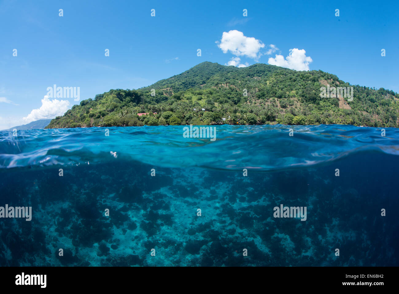 Un over in vista della barriera corallina al di sotto della superficie dell'oceano e dell'isola di Vulcano Pura nello stretto di Pantar, Alor, Indonesia Foto Stock