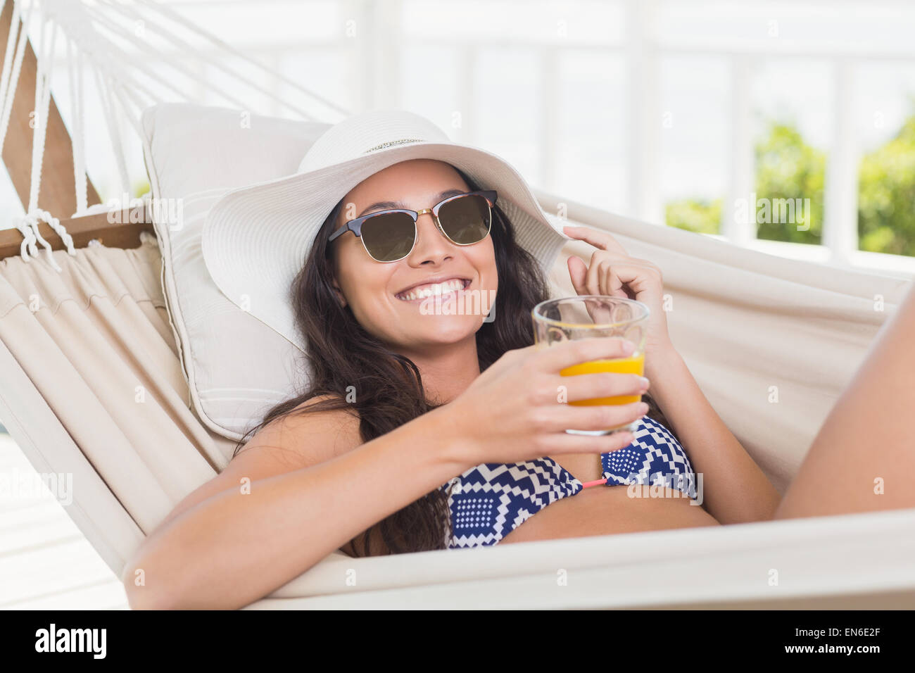 Bella bruna relax su una amaca e bere il succo d'arancia Foto Stock