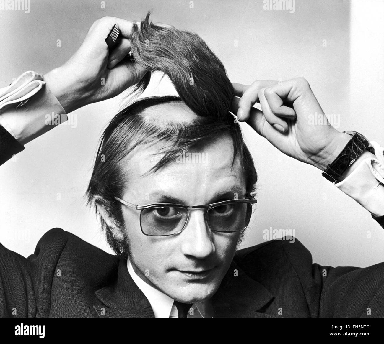 Il signor Graham George attaccando un pezzo di capelli alla rasata patch calve sulla cima della sua testa. Il 28 marzo 1970. Foto Stock