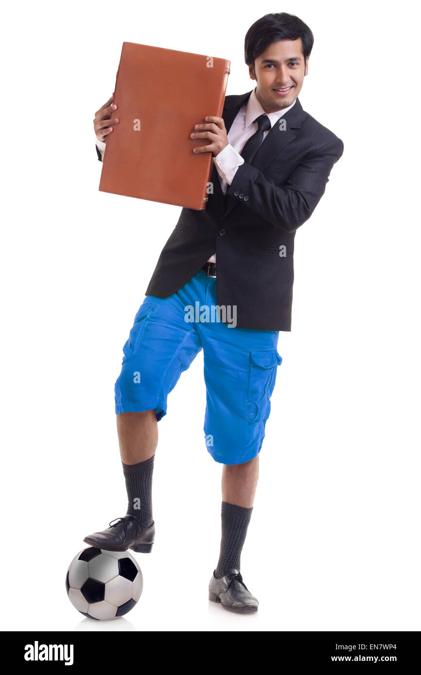 Ritratto di giovane sorridente uomo in piedi con un piede su un campo di calcio e valigetta di contenimento Foto Stock