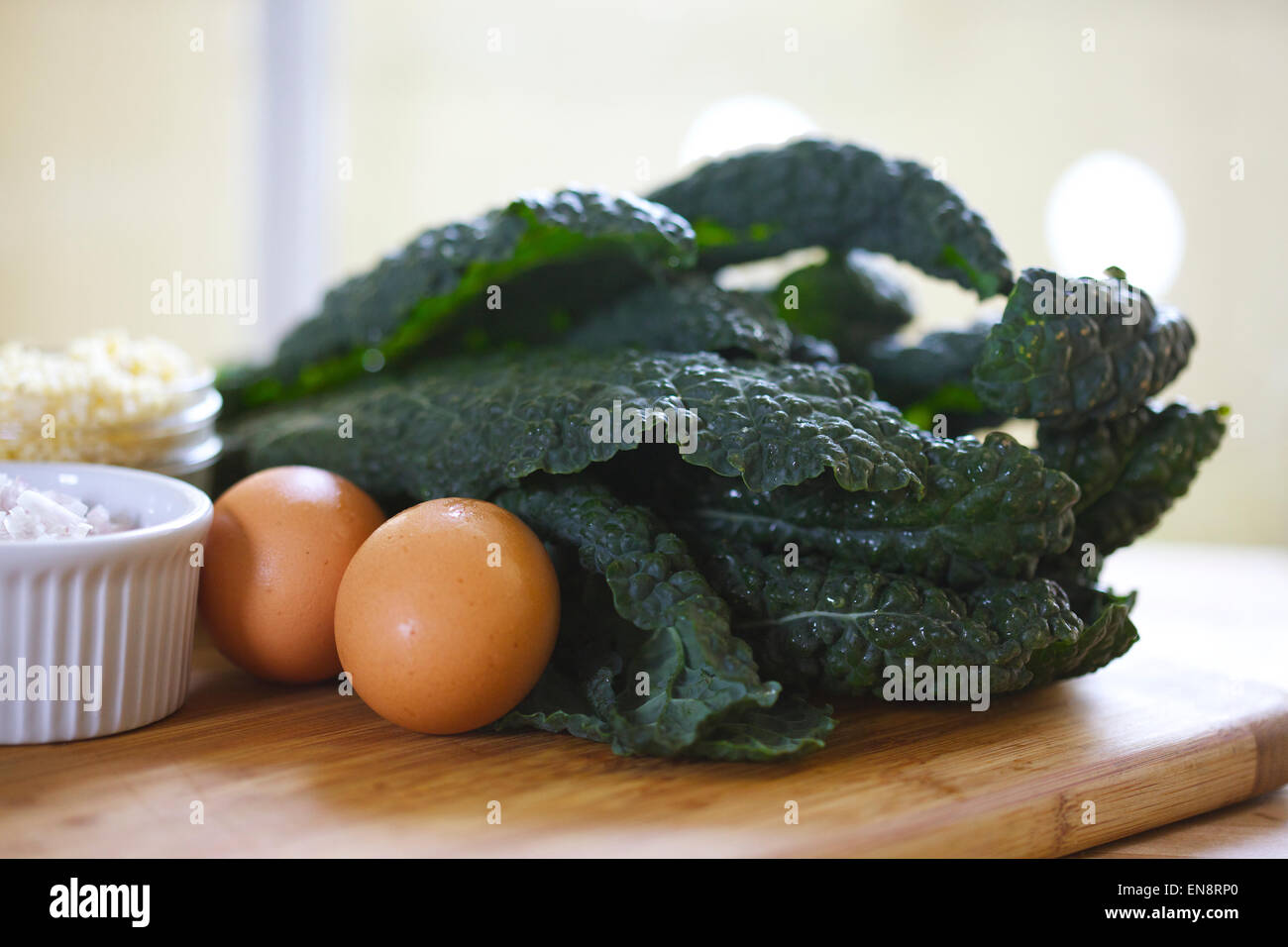 Due uova e un mazzetto di lavato lacinato kale disposti su un tagliere. Foto Stock