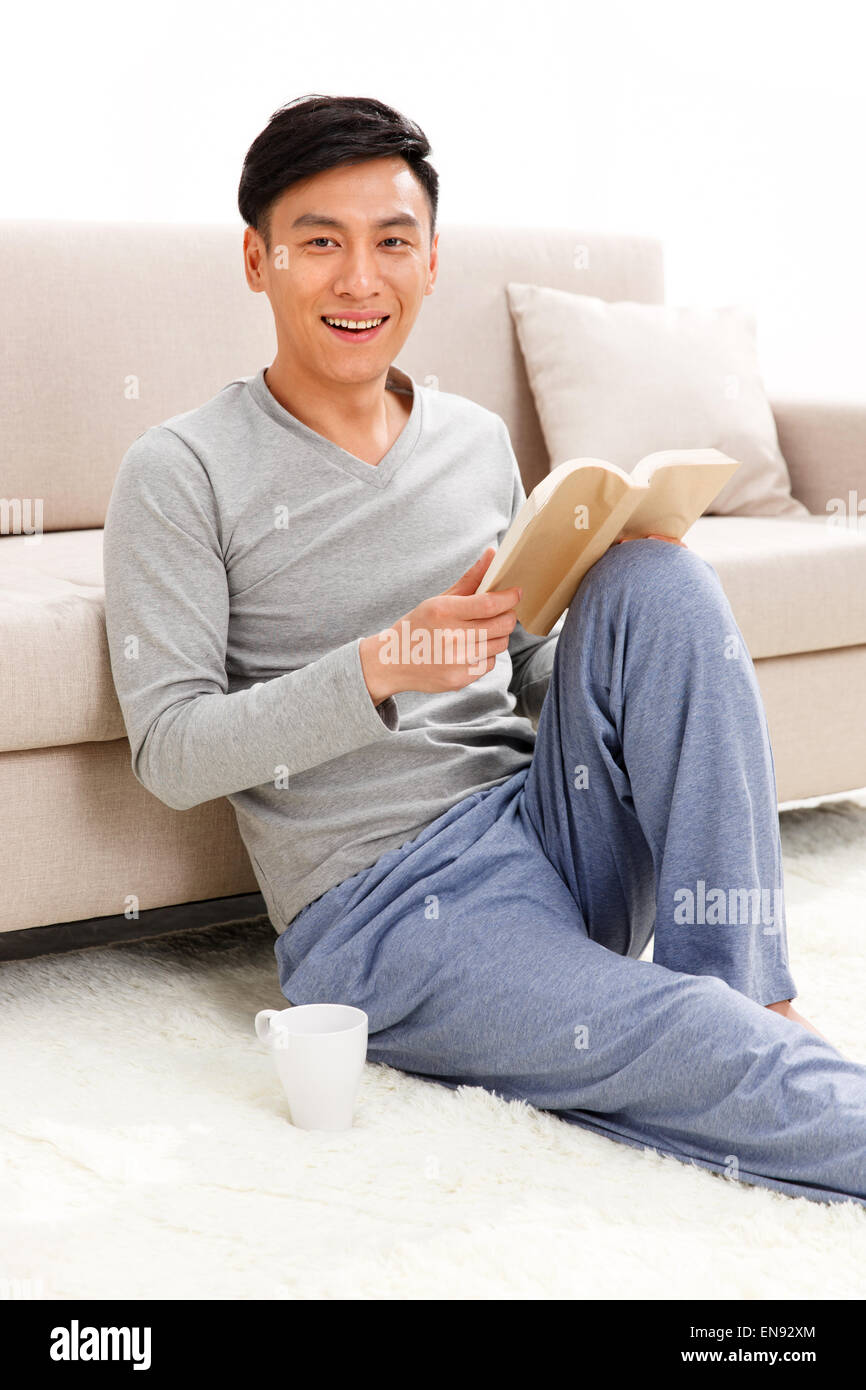 Giovane uomo seduto sul pavimento e leggere un libro Foto Stock